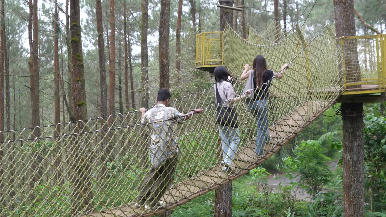 Young Asian Friends Crossing Rope Bridge in Forest Adventure