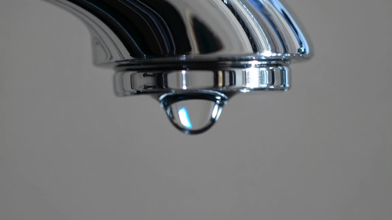 Close-up shot of a chrome faucet with a droplet, captured from a low angle