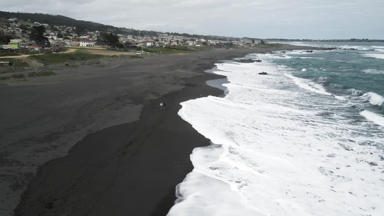 Aerial View of a Black Sand Beach with Ocean Waves and Coastal Town