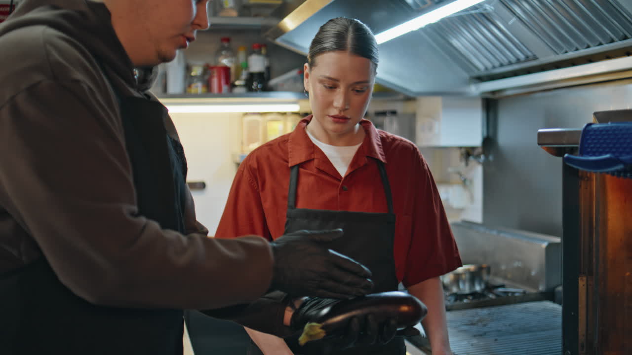 Restaurant worker discussing recipe with man chef in gloves at modern kitchen