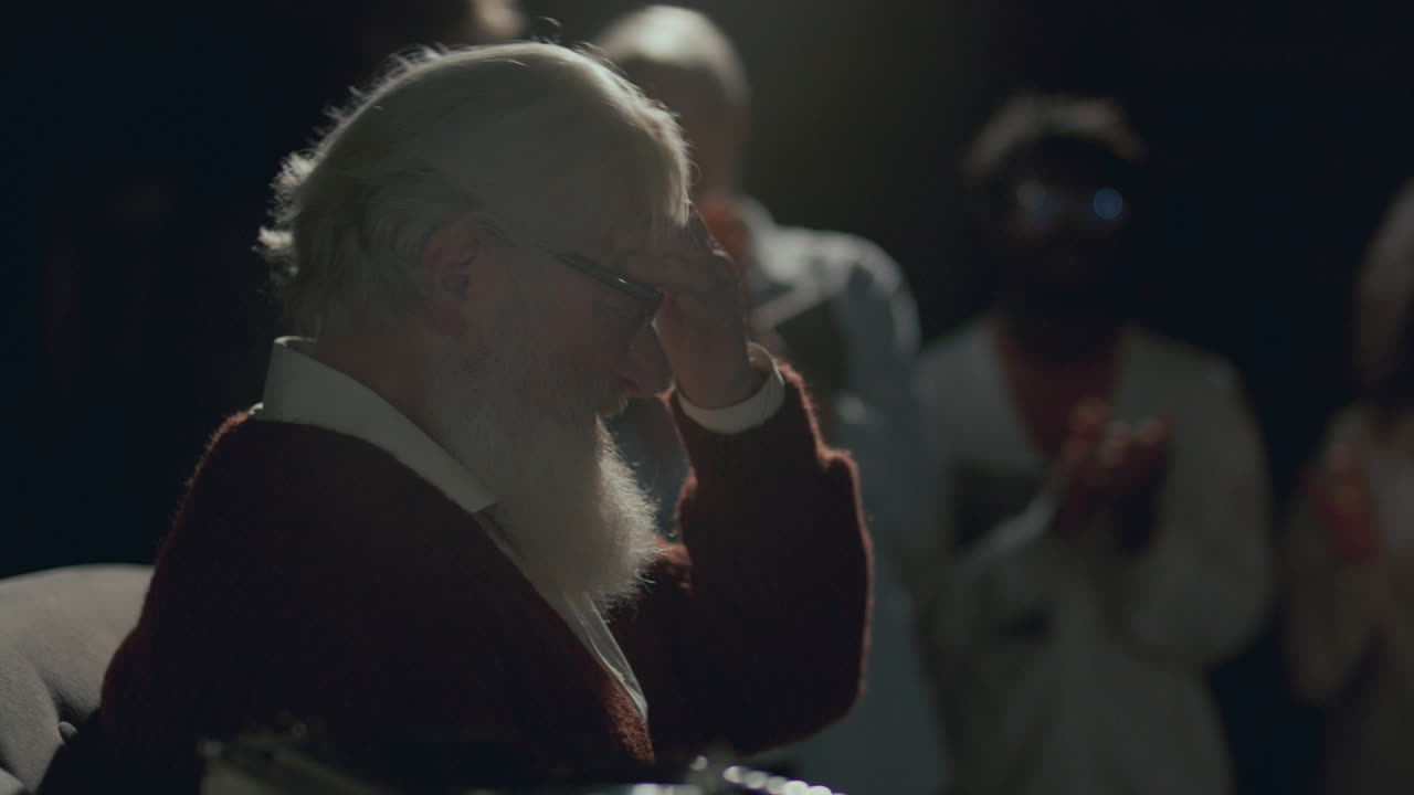 노인 작가가 책 발표 행사에서 관객들에게 감정적으로 감사하고 있습니다.