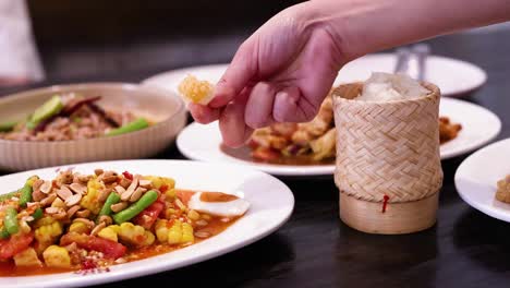 hand serving sticky rice with colorful dishes