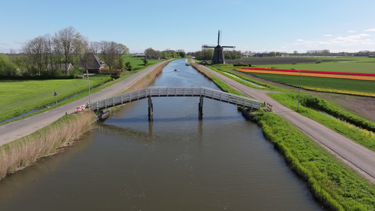 Flyfoto av båt som seiler på elv flankert av tulipaner og vindmølle, Nederland