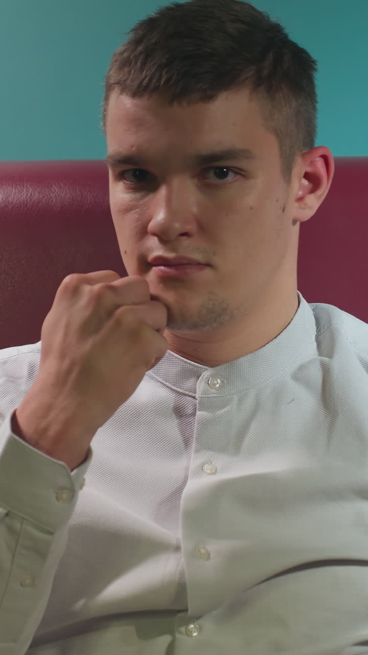 색 소파에 앉아있는 색 셔츠를 입은 남자의 클로즈업. 큐 스틱이 손으로 빌리어드 공을 던지면서 그의 에 기울어져 있습니다. 부드러운 조명은 그의 집중된 분위기를 강조합니다.