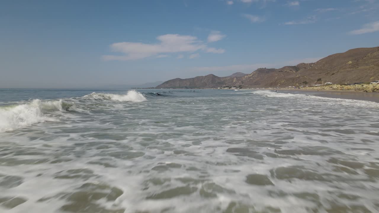 Una ripresa con drone che sfiora le onde e si alza sopra un gruppo di surfisti