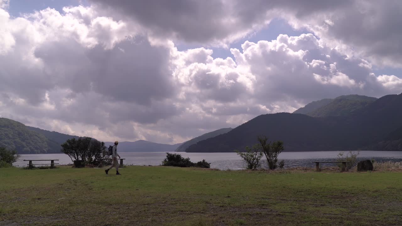 plano general de un excursionista masculino caminando por un hermoso paisaje natural frente a un lago tranquilo
