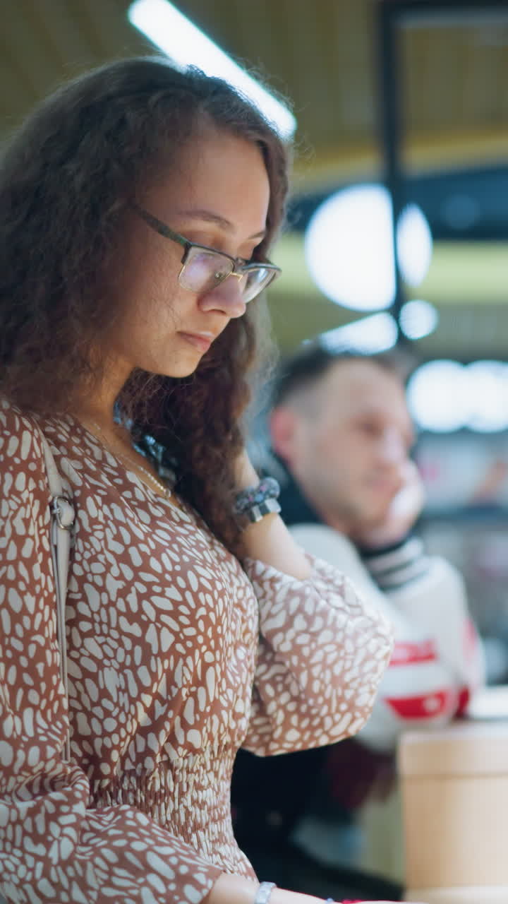 vista lateral de una mujer con un vestido vintage de pie frente a la tienda sosteniendo un papel de menú, mirando contemplativamente las opciones mientras otra persona a su lado descansa la cabeza sobre la mano pensativa