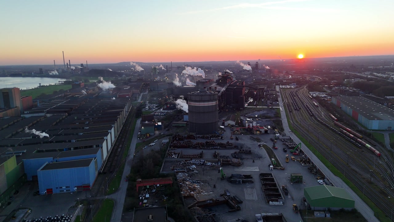 Darker sunrise aerial revealing riverfront industrial corridor stretching toward a distant coking plant