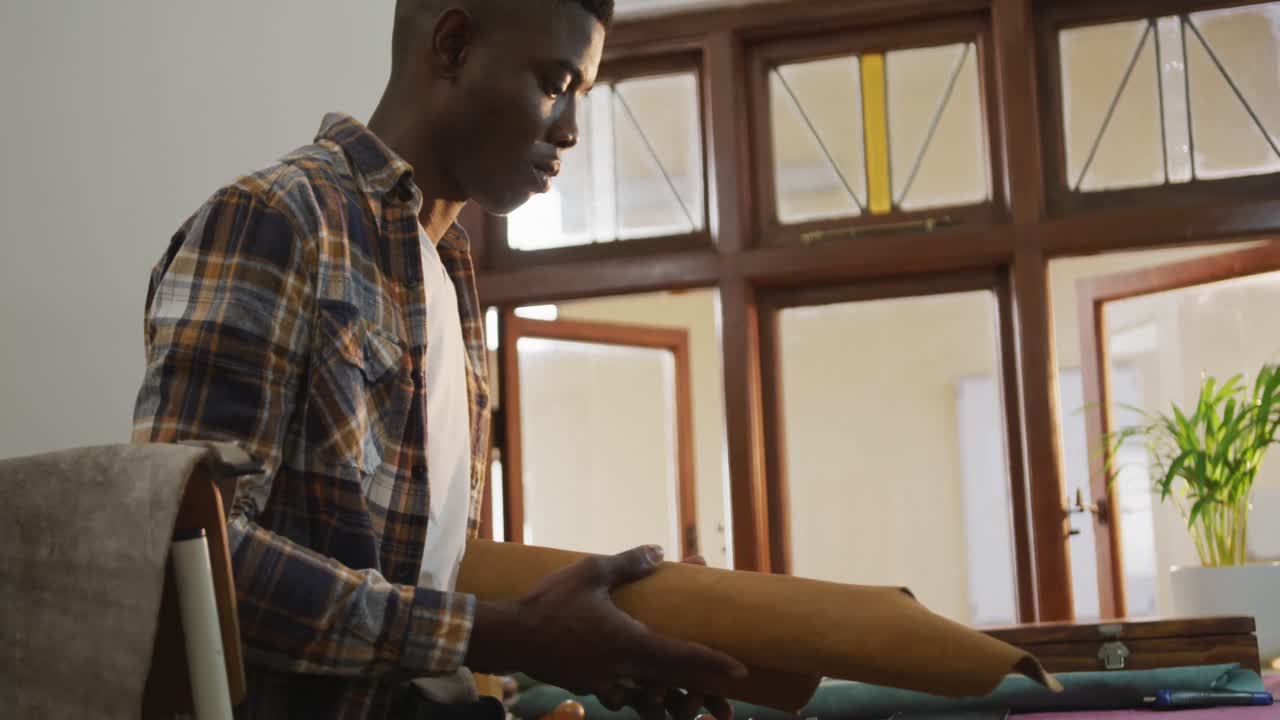 African american craftsman holding rolls of leather in leather workshop