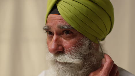 close up studio shot of senior sikh man with beard using salai needle when putting on turban against plain background 2