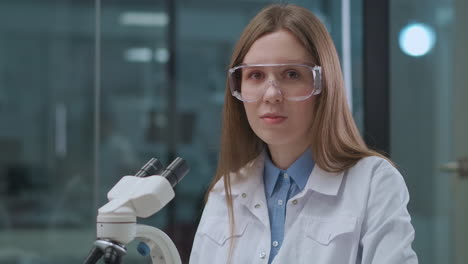 El-Laboratorio-Técnico-De-Una-Joven-Está-Trabajando-Con-Microscopio-Y-Mirando-A-La-Cámara.-Retrato-De-Una-Profesional-De-La-Salud-En-Un-Hospital-O-Instituto-Científico.