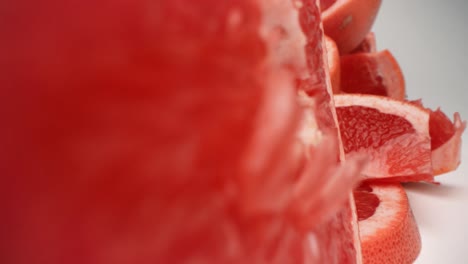 grapefruit slice spins and falls over into pile of grapefruit closeup pull away through the center of grapefruit section product food video 4k