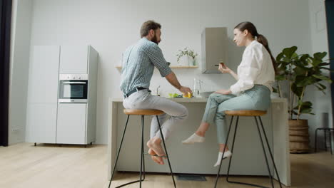 Loving-Couple-Chatting-And-Having-Lunch-Together-Sitting-On-Stool-In-A-Modern-Kitchen