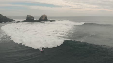 Aerial-Shot-of-Pro-Surfer-on-a-pink-board-riding-big-wave-in-Pichilemu,-Chile-4K