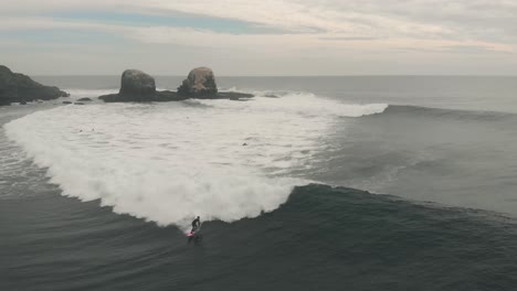 Toma-Aérea-De-Un-Surfista-Profesional-En-Una-Tabla-Rosa-Montando-Una-Gran-Ola-En-Pichilemu,-Chile-4k