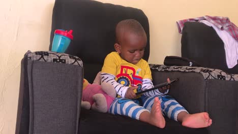 a young african boy plays on a tablet computer, while sitting in a chair in his home