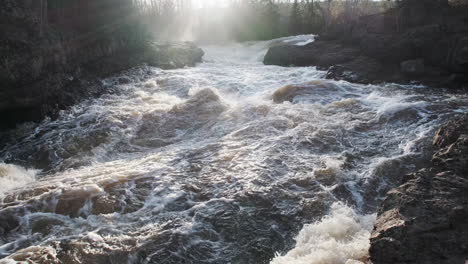 slow pan and lens flare, raging rocky river rapids with water spray at sunset
