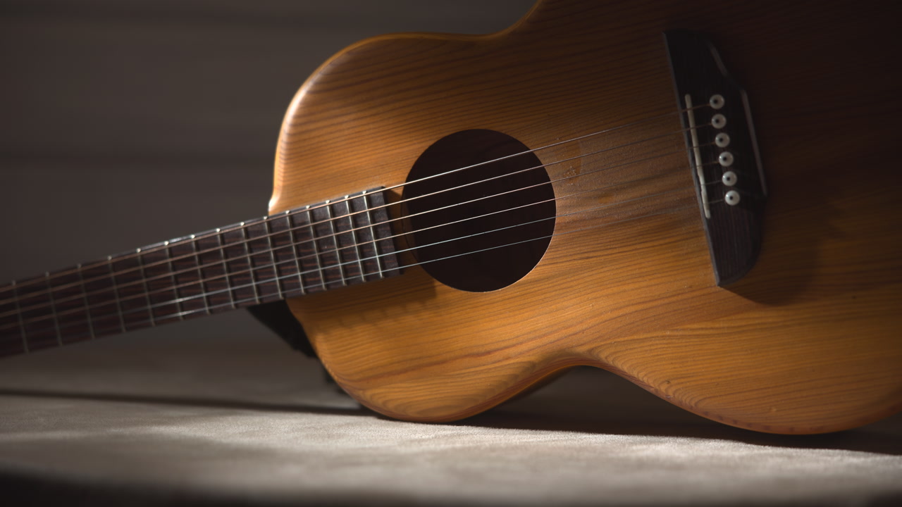 Angled Acoustic Guitar Under Spotlight, Dramatic Chiaroscuro And Deep Shadows, Warm Lacquered Body, Wide . Media