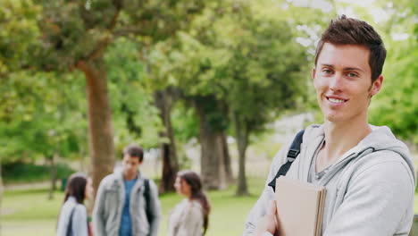 man reading a book before looking at the camera while smiling as he stands in a park