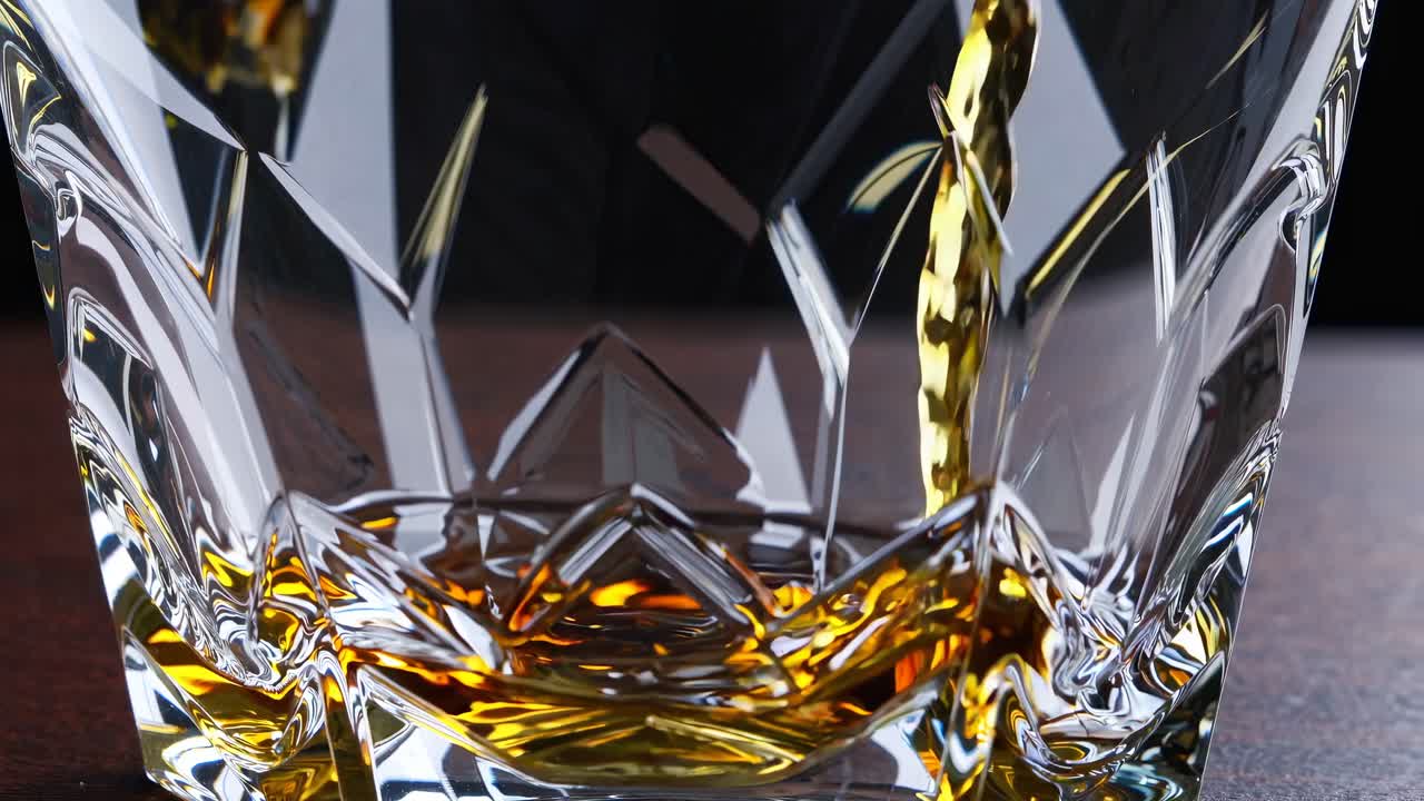 Close-up, low-angle shot of whiskey being poured into a faceted glass, capturing the rich amber