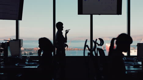 Silueta-De-Un-Hombre-De-Negocios-Usando-Un-Teléfono-Inteligente-Con-Una-Llamada-Telefónica-Charlando-Por-Un-Teléfono-Móvil-Mirando-Por-La-Ventana-Un-Ejecutivo-Corporativo-Discutiendo-Las-Ventas-Trabajando-Hasta-Tarde-En-Una-Oficina-Ocupada