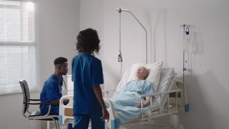 a team of african ethnic group doctors a man and a woman talk to an elderly male patient. a doctor and a nurse talk to a bedridden patient in a hospital ward