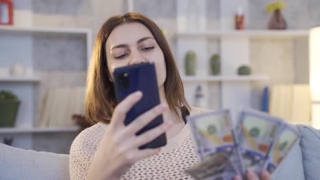 Happy-young-woman-with-money-looking-at-her-smartphone,-making-money,-spending-money.