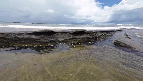 Beautiful-landscape-shot-of-small-waves-crashing-over-large-rocks-of-the-Tibau-do-Sul-beach-near-Pipa,-Brazil-in-Rio-Grande-do-Norte-during-a-cloudy-summer-day