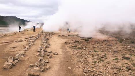 people photographing fumarole with smoke from ground in a desert environment