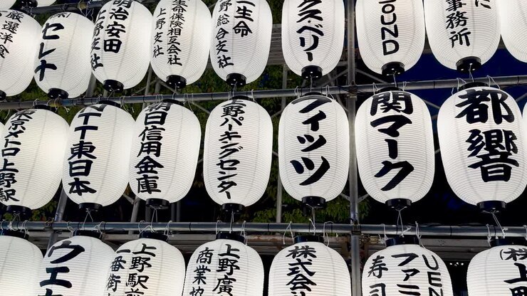 File di lanterne di carta bianche illuminate con calligrafia kanji nera ondeggiano dolcemente di notte.