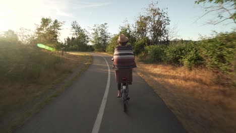 Chica-En-Bicicleta-A-Lo-Largo-De-Un-Carril-Bici-Disparado-Desde-Atrás-En-Un-Cardán-Hacia-La-Puesta-De-Sol