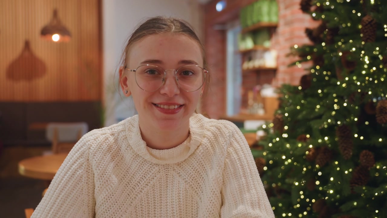 Giovane donna che scrive al bar e sorride alla fotocamera con un albero di Natale