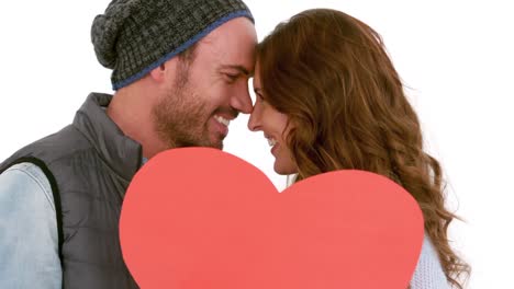 una joven pareja cubriendo su cara con un corazón de almohada