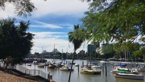 View-over-the-river-marina-towards-the-Story-Bridge-in-downtown-Brisbane,-Australia,-as-a-pair-of-jetskis-speed-up-the-river