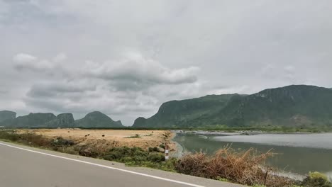 driving along a road next to a lake with mountainous hills in the background in thailand