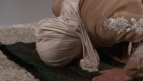 close up of muslim woman wearing hijab at home praying kneeling on prayer mat