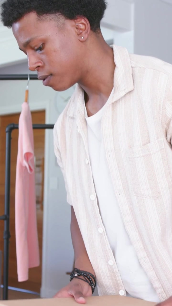 Vertical video: Checking planner and tapping pen, man in striped shirt preparing packages at table