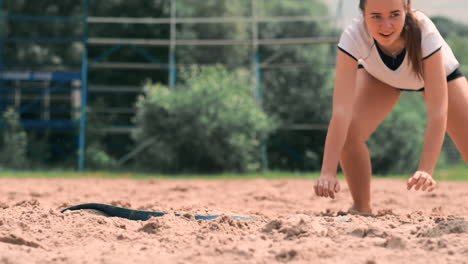 una joven atleta se sumerge en la arena y ahorra un punto durante un partido de voleibol de playa. una alegre chica caucásica salta y se estrella en la arena blanca durante un torneo de voleibal de playa.