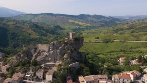 drone shot flying towards a medieval castle on the side of a cliff revealing the small village below and the mountains