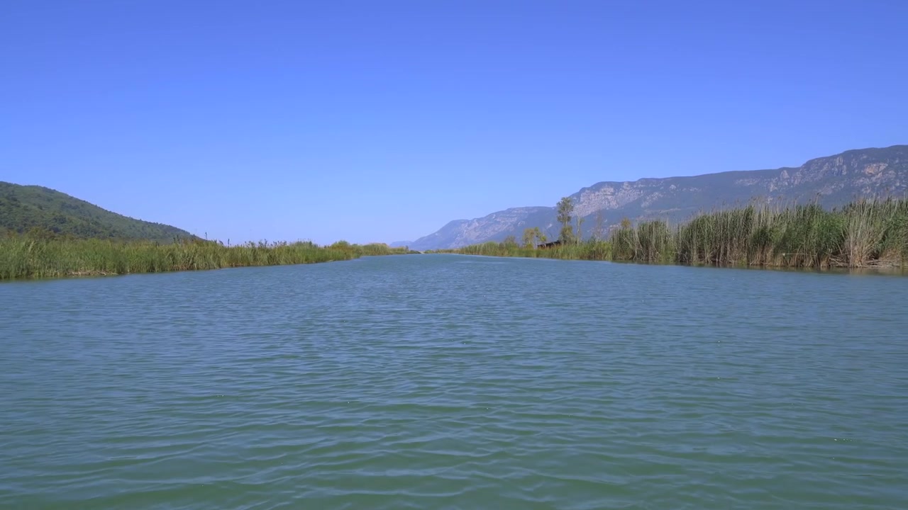Bateau naviguant sur une rivière calme entourée de roseaux et de montagnes