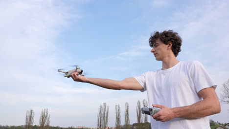 Hombre-Joven-Y-Dron,-Aterrizando-Un-Pequeño-Avión-Quadcopter-En-La-Mano-Usando-El-Controlador-En-Otra-Cámara-Lenta