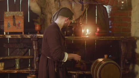 el barman vierte cerveza artesanal y mira hacia atrás con miedo en la posada. el sirviente del ladrón en la gorra roba alcohol en el sótano de la taberna. el asistente preocupado en la casa pública medieval