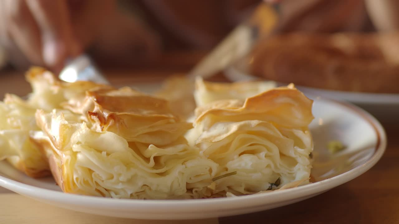 Close-up of hands cutting a flaky pastry