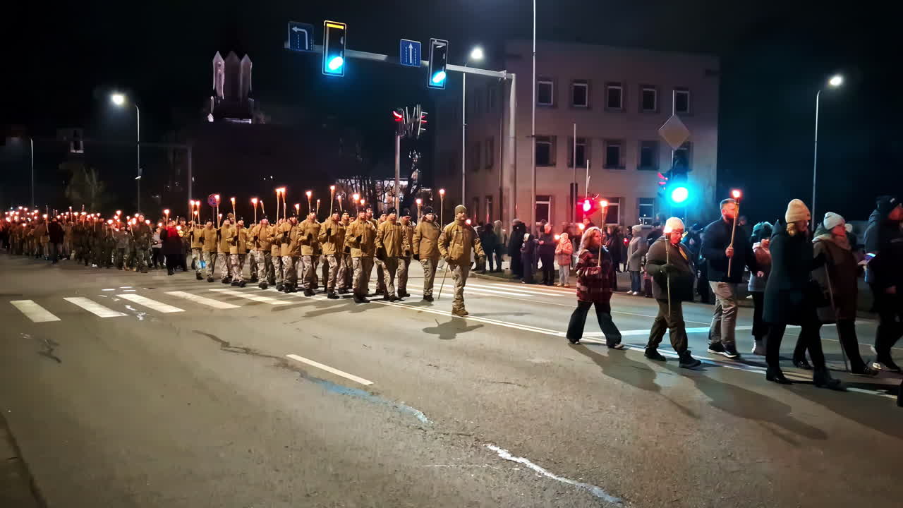 Lāčplēsis Day torchlight procession crossing a city street at night in Jelgava, Latvia