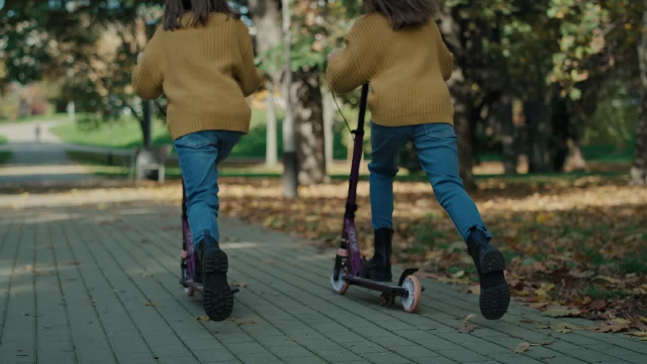 Rear view of caucasian child siblings having fun in the woods while driving a push scooter.