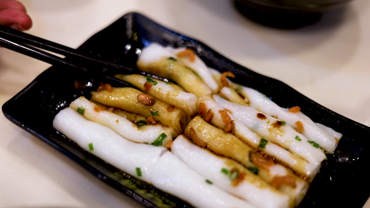Chopsticks lifting noodles from a black plate