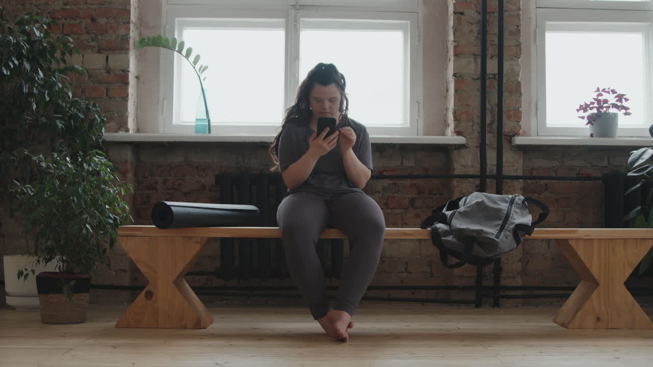 Young Woman With Down Syndrome Using Smartphone At Yoga Studio