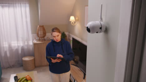 woman using a tablet to view security camera feed in a living room.