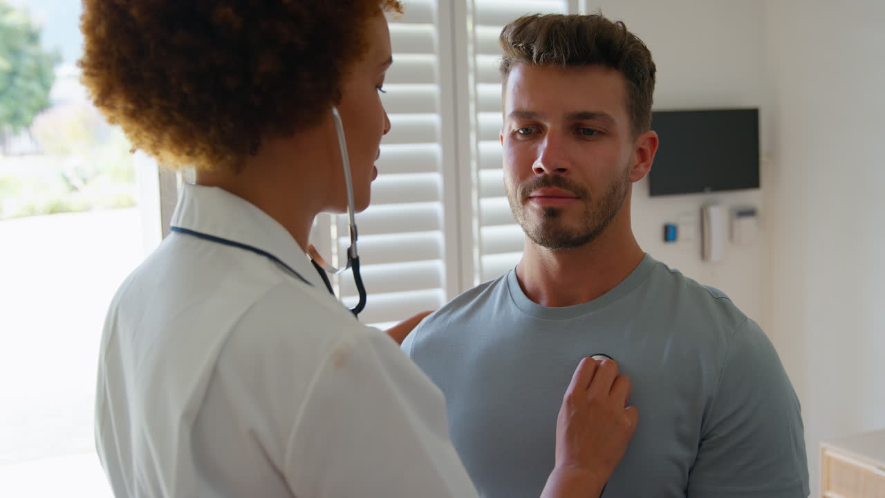 Female Nurse Wearing Uniform Listening To Male Patient's Chest In Private Hospital Room