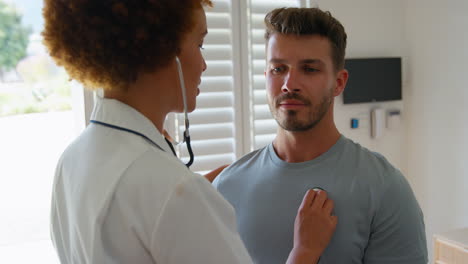 female nurse wearing uniform listening to male patient's chest in private hospital room